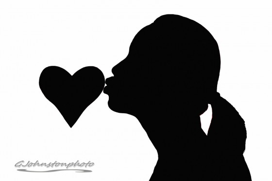 Silhouette of woman kissing a heart.