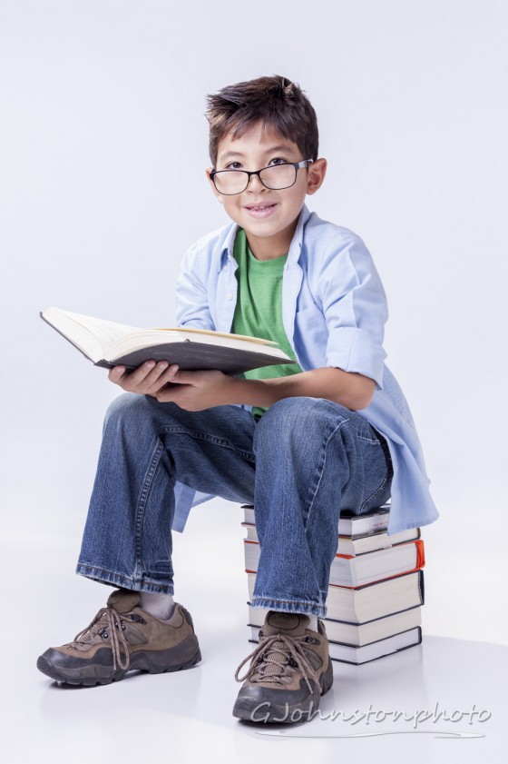Boy reads book while on a stack of books.
